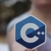 Close-up of person holding a C++ logo sticker, blurred background.