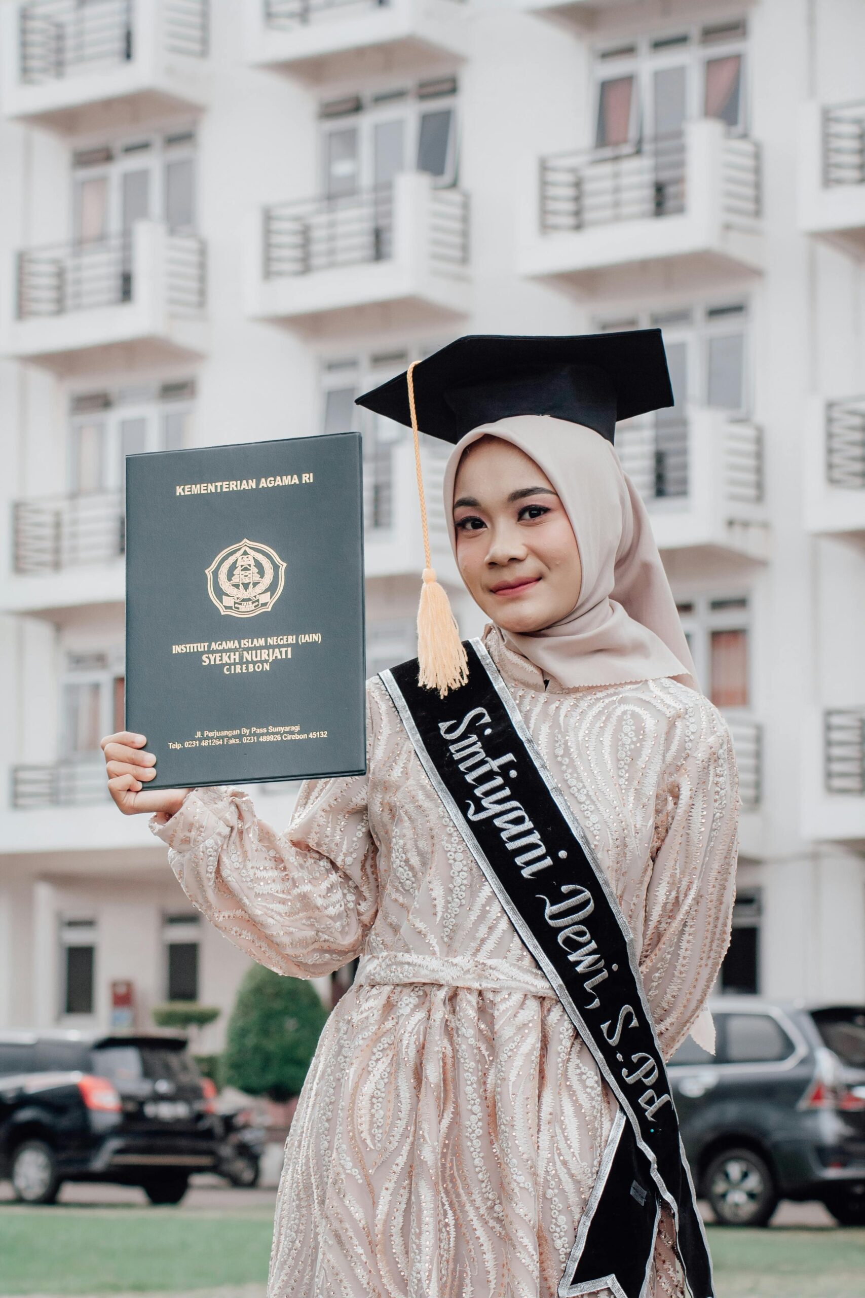 Home Young Muslim woman in hijab celebrates graduation outdoors in Indonesia.