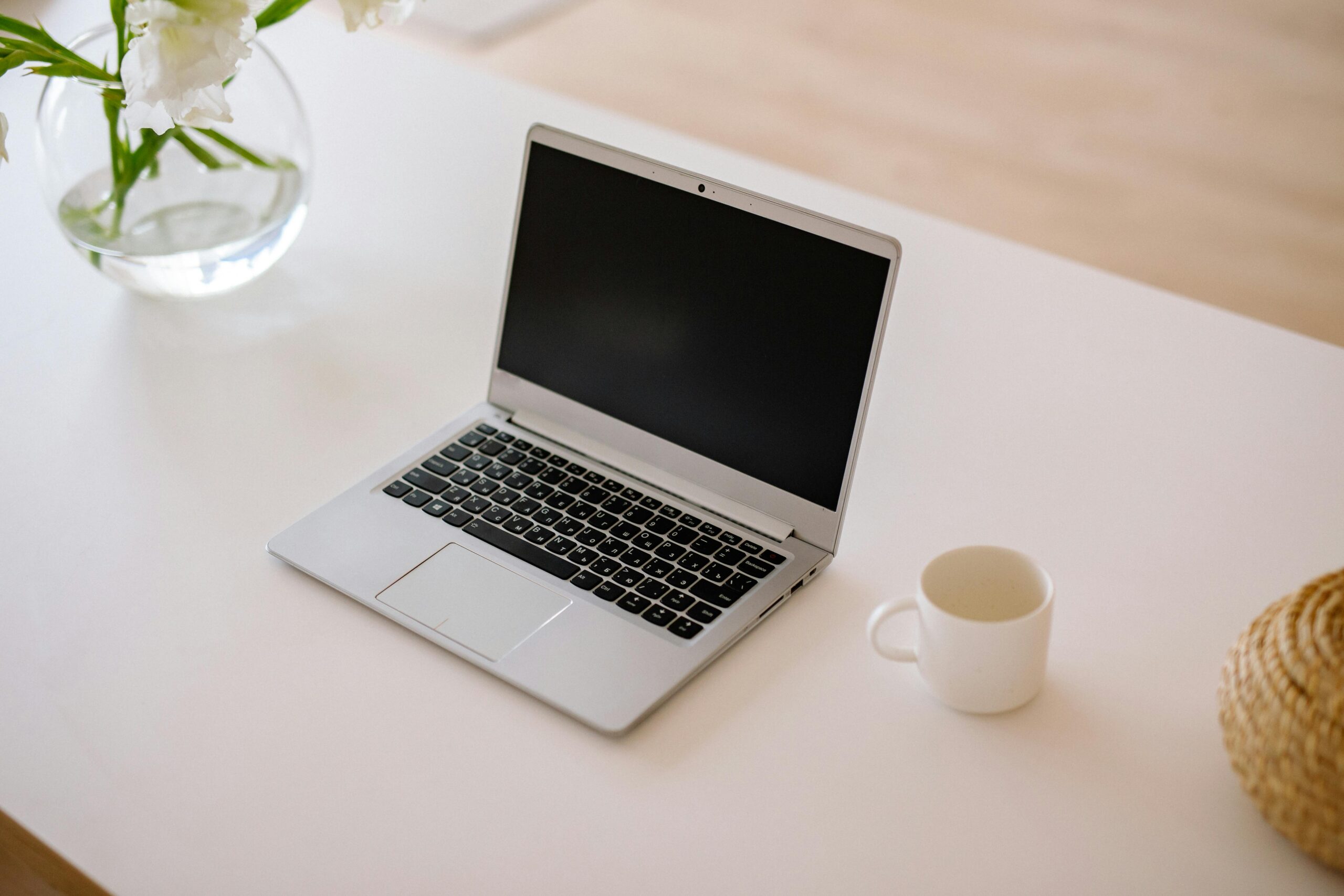 Home A minimalist workspace with an open laptop, coffee mug, and vase on a bright indoor table.